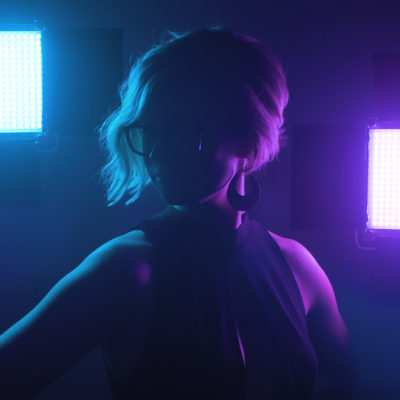 Yvois is backlit with blue and purple lights, shining through her hair and dangling earring